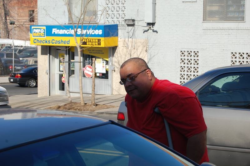 Un voluntario con camisa roja se apoya en la puerta de un auto en una calle del Bronx durante un reparto de donaciones.