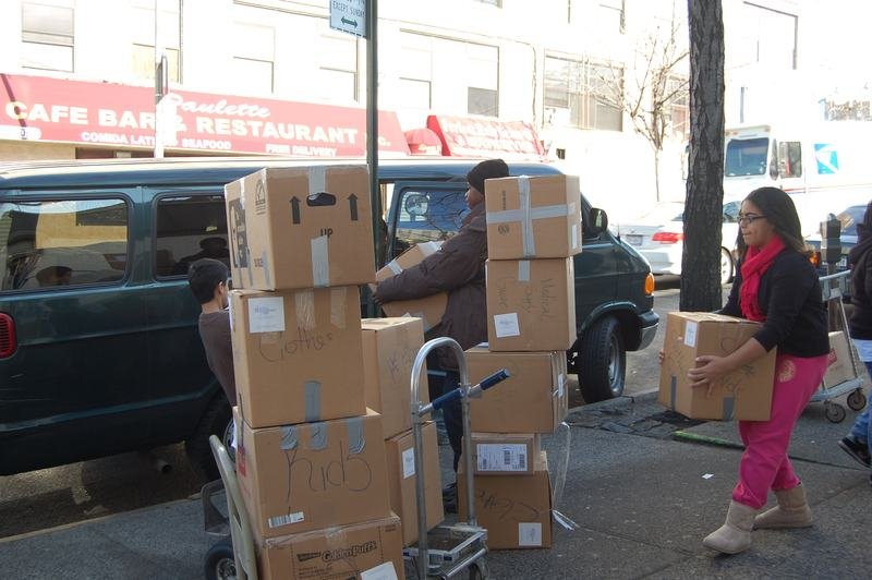 Voluntarios trasladan cajas de donaciones apiladas por una calle del Bronx junto a una camioneta estacionada.