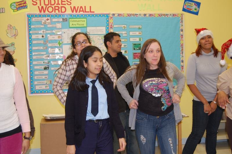 Mentores y mentoreados bailan frente al mural de vocabulario del aula, varios con gorros de Papá Noel.