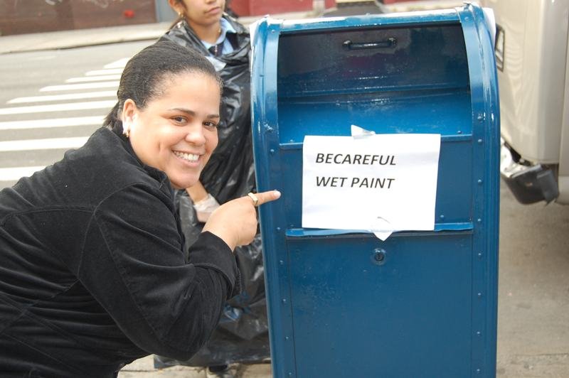 Una voluntaria señala un cartel escrito a mano de pintura fresca pegado a un buzón recién pintado.